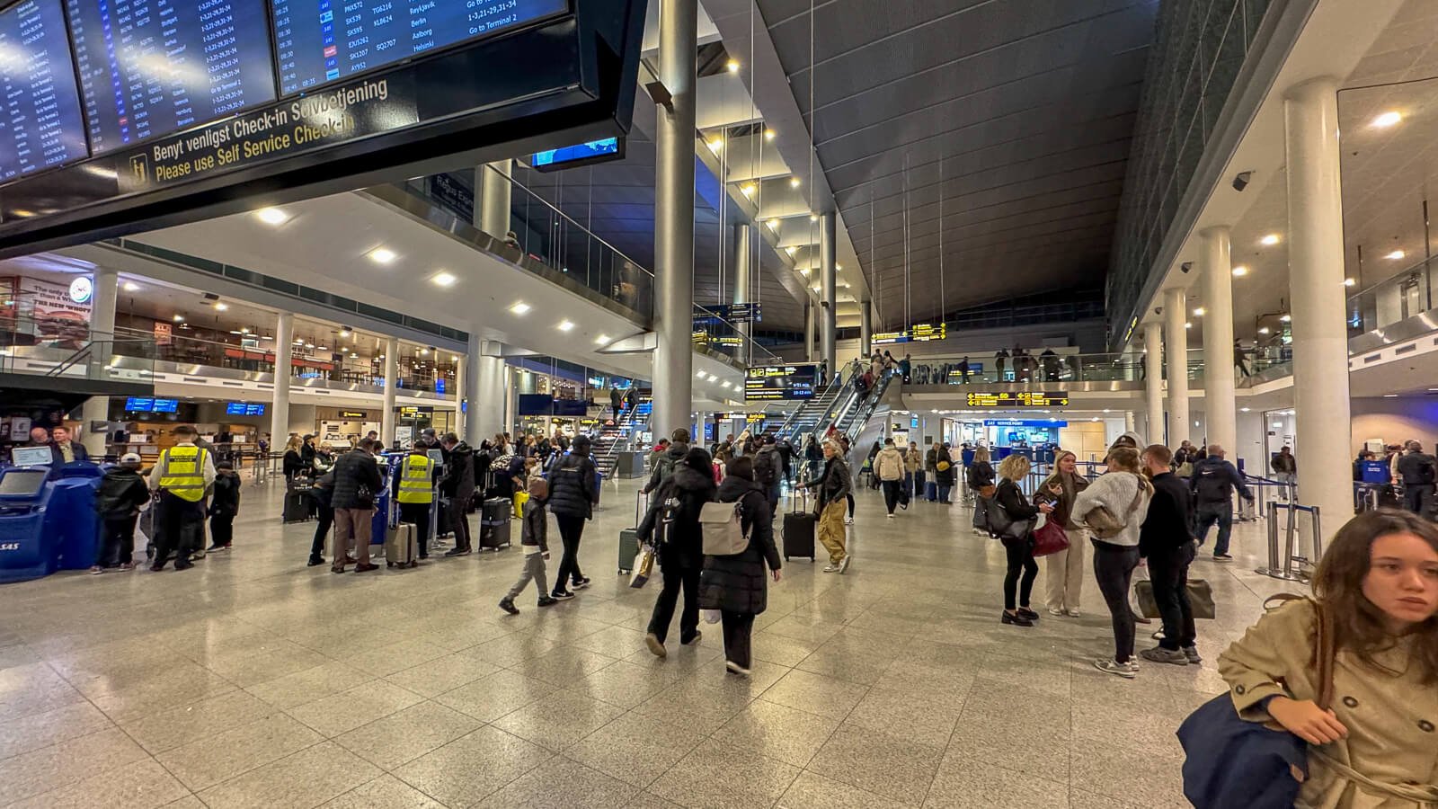 Københavns Lufthavn med rejsende, check-in-automater og informationstavler i afgangshallen.